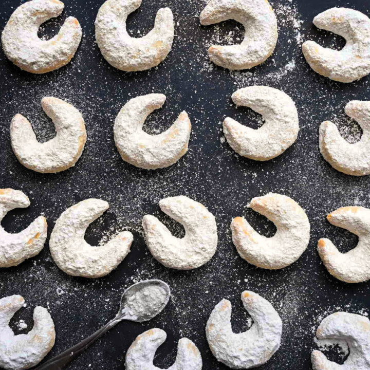 Des sablés a la vanille recouverts de sucre glace, sur un fond noir avec une petite cuillère.