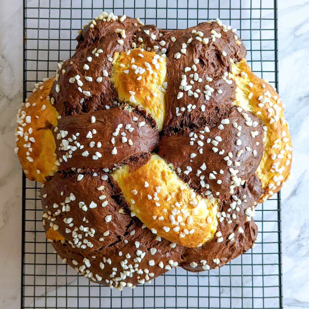 Une brioche tressée chocolat vanille de forme ronde sur une grille de refroidissement noire, sur un plan de travail de couleur marbré.
