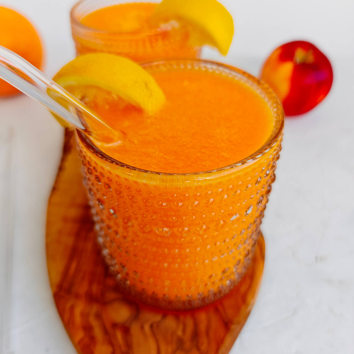 Deux verres de jus détox carottes, orange et gingembre sur une petite planche de bois, sur un fond blanc.