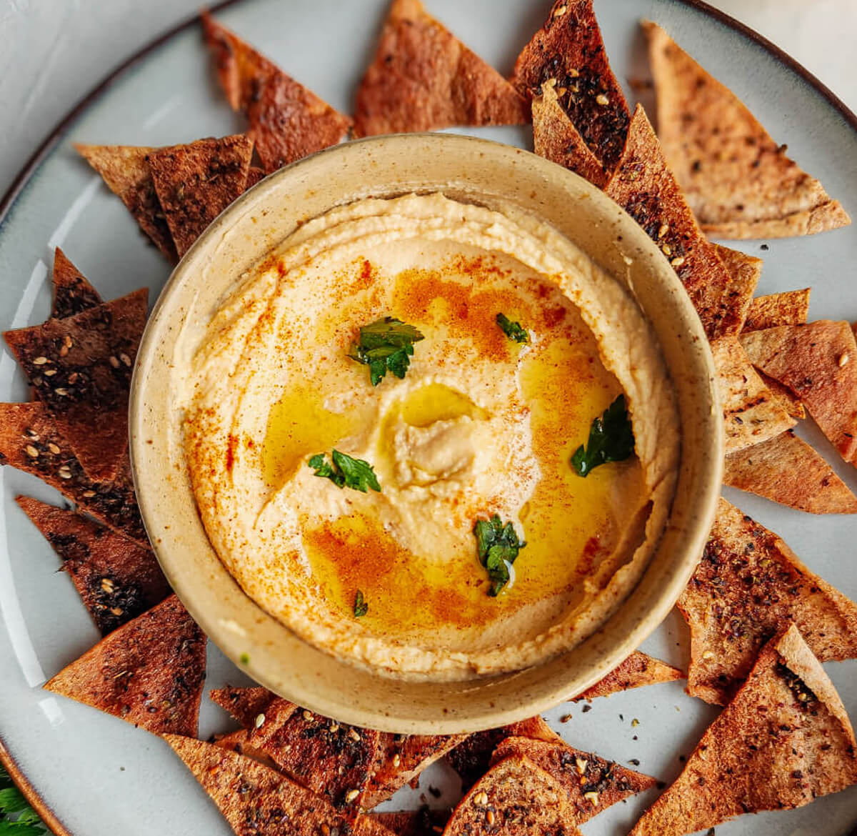 Un bol de houmous libanais authentique garnis d'huile d'olive, du persil frais et du prapika. Des chips de pita sur le coté.