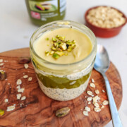 Un pot en verre contenant une préparation d'overnight oats sur une planche en bois, sur un fond blanc.