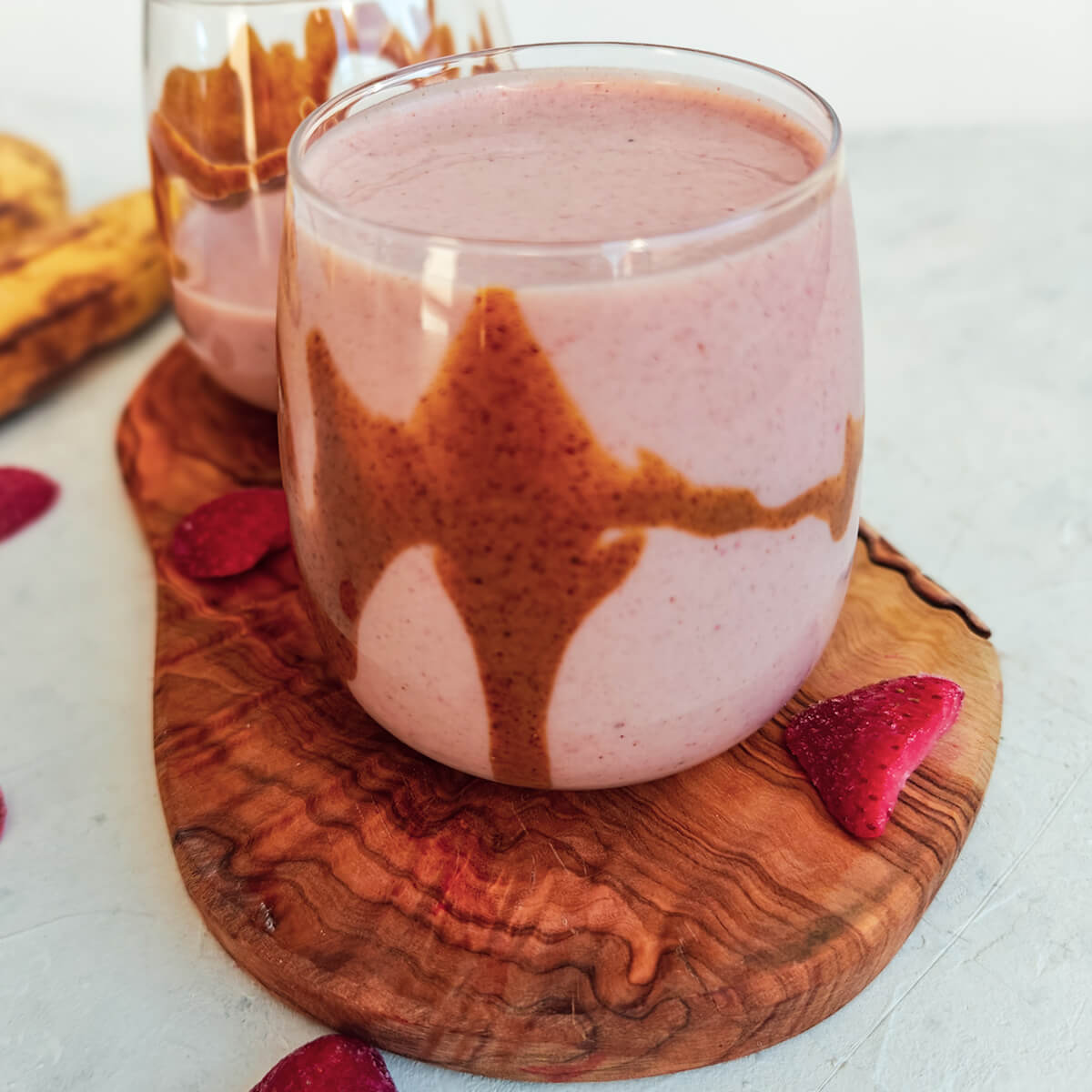deux verres de smoothie fraise banane sur une planche de bois, sur un fond blanc avec des fraises.