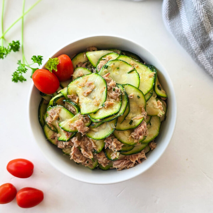 Un bol contenant des courgettes crues en rondelles avec du thon, tomates cerises, sur un fond blanc.