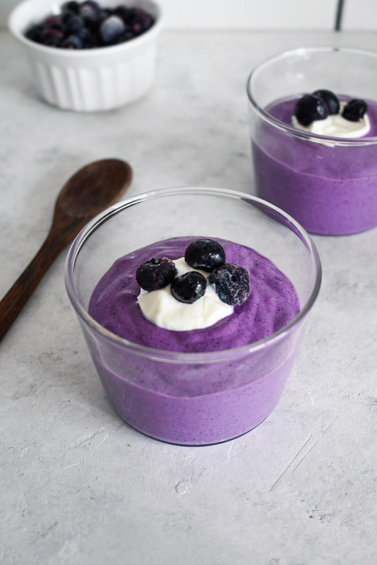 Porridge avoine-myrtilles en verrines sur fond gris clair.