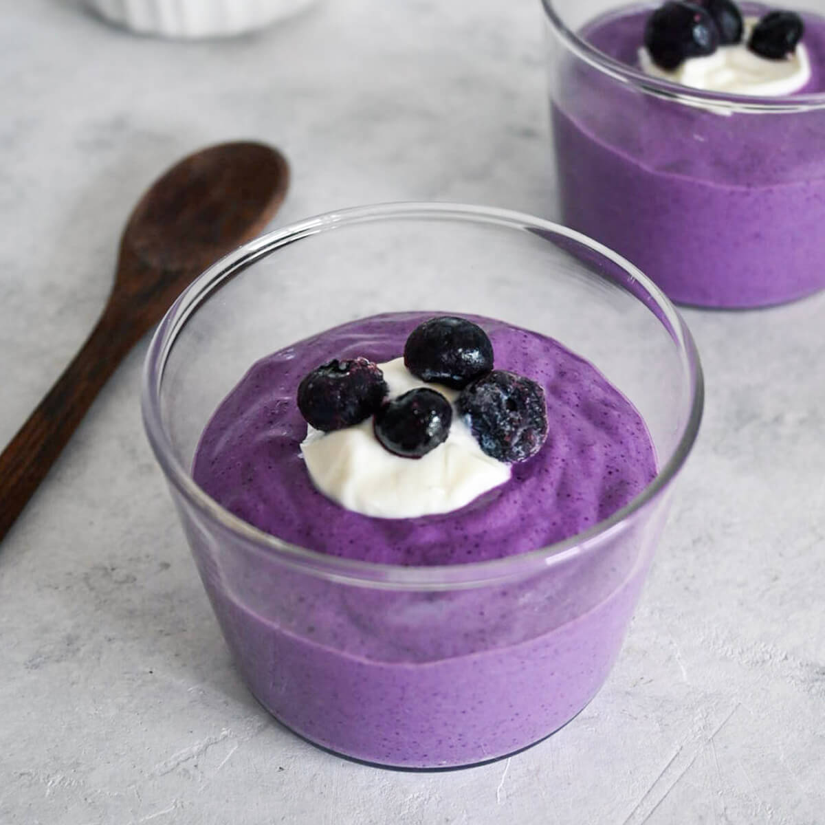 Porridge avoine-myrtilles en verrines sur fond gris clair.