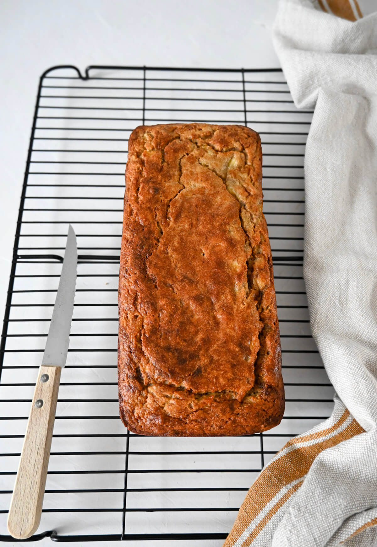 Un banana bread sur une plaque de refroidissement noire, couteau et torchon sur le coté.