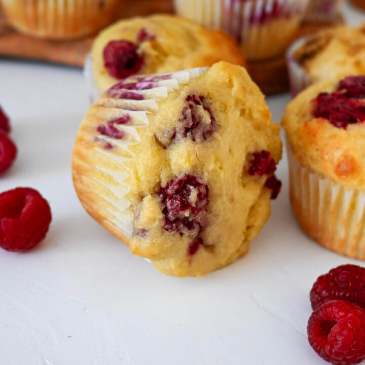 Un muffin framboise citron sur le côté, framboises fraîches sur le côté, sur un fond blanc.