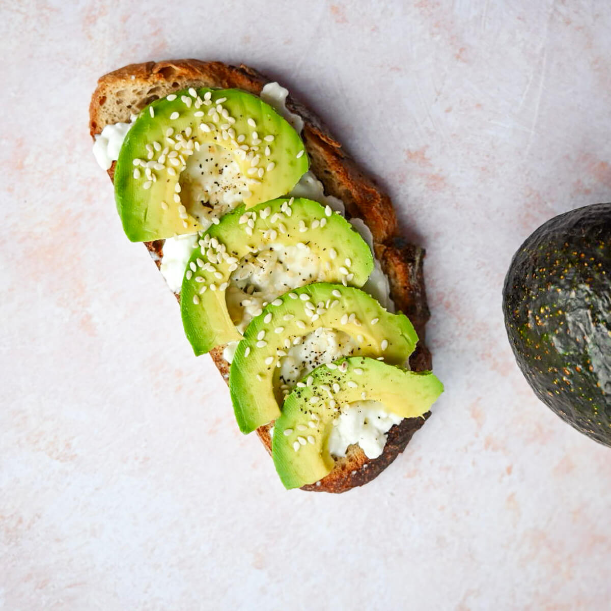Une tartine d'avocat cottage cheese sur un fond rose clair.