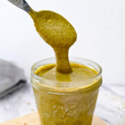 Un pot contenant de la crème de pistachem avec une cuillèere, sur une planche de bois.