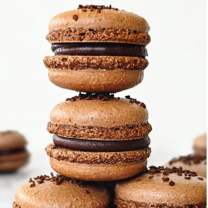 Des macarons au chocolat empilés les uns sur les autres, sur un fond blanc.