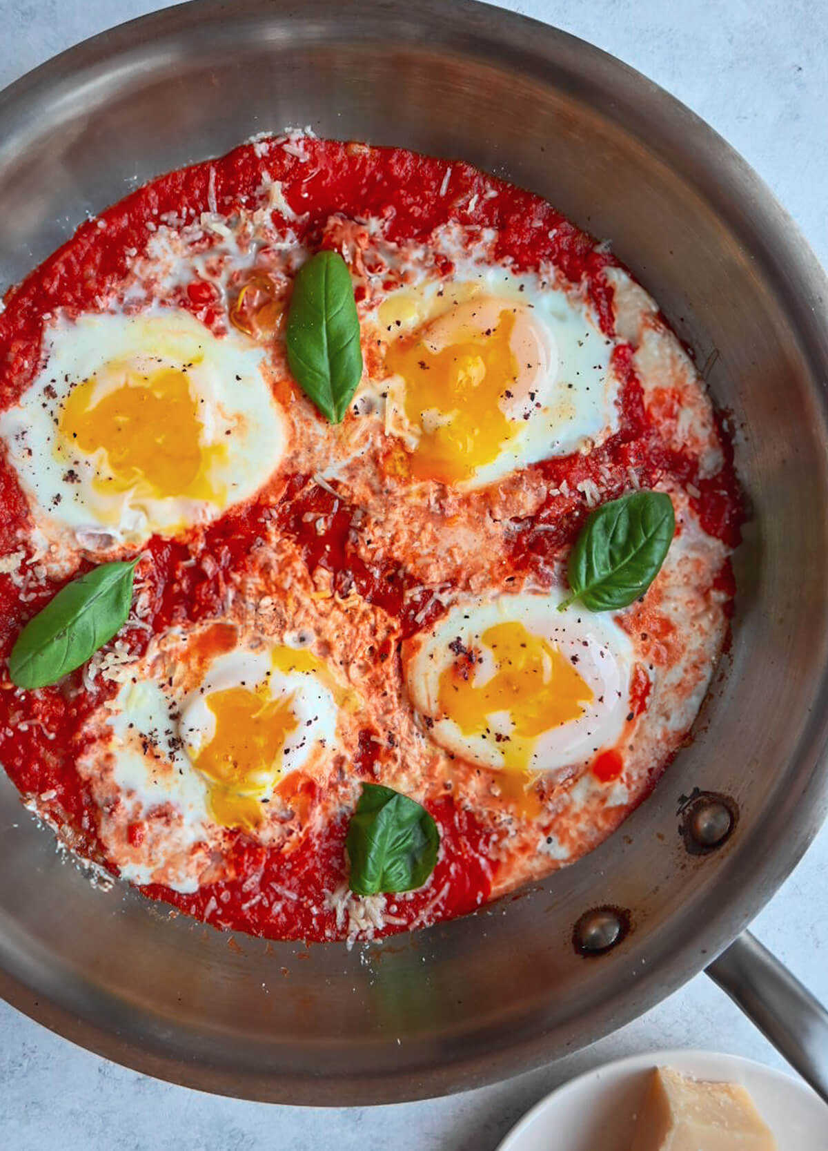 Des œufs à la tomate dans une poêle en inox, parmesan sur le côté.