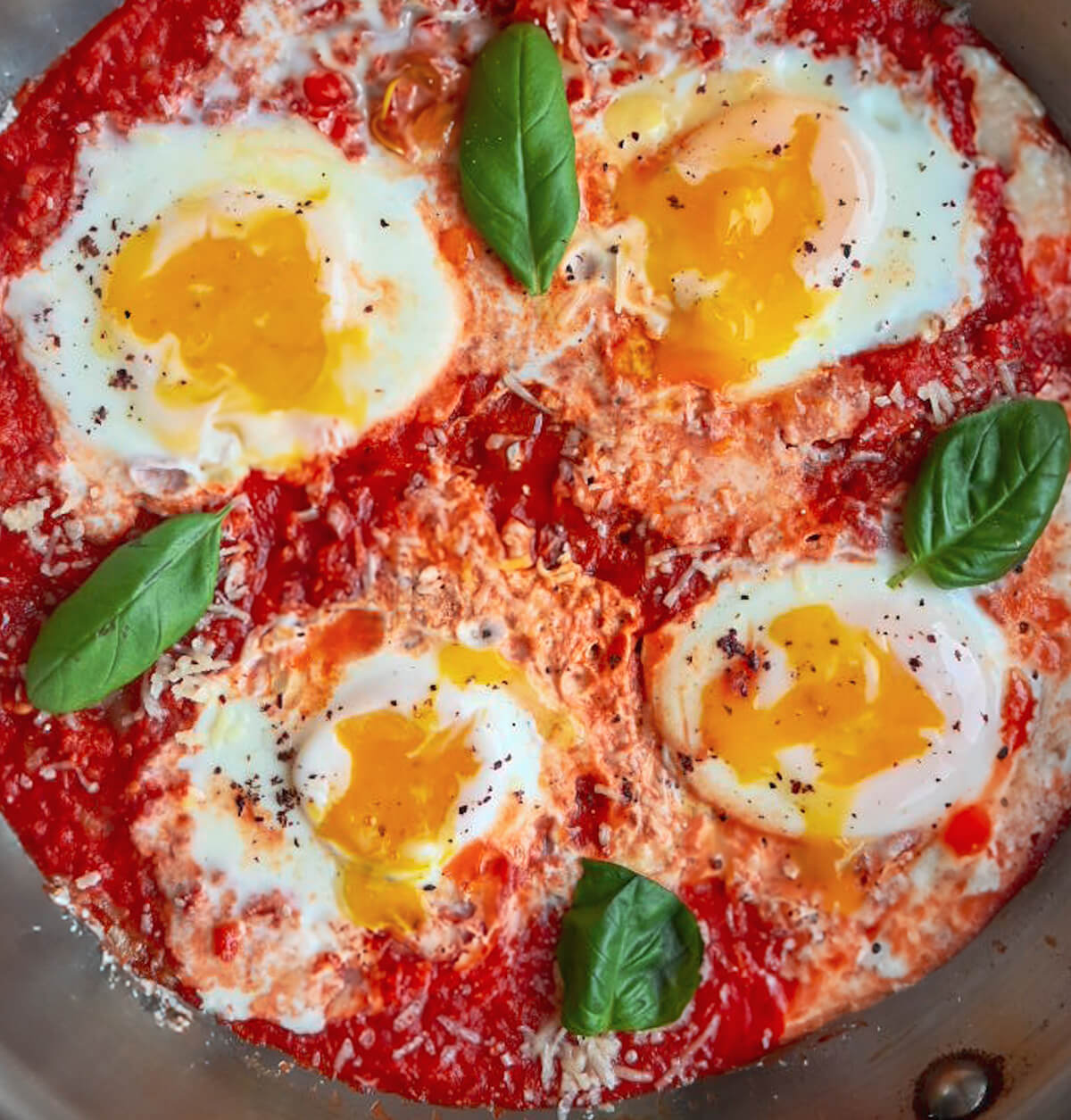 Des œufs à la tomate dans une poêle en inox, parmesan sur le côté.