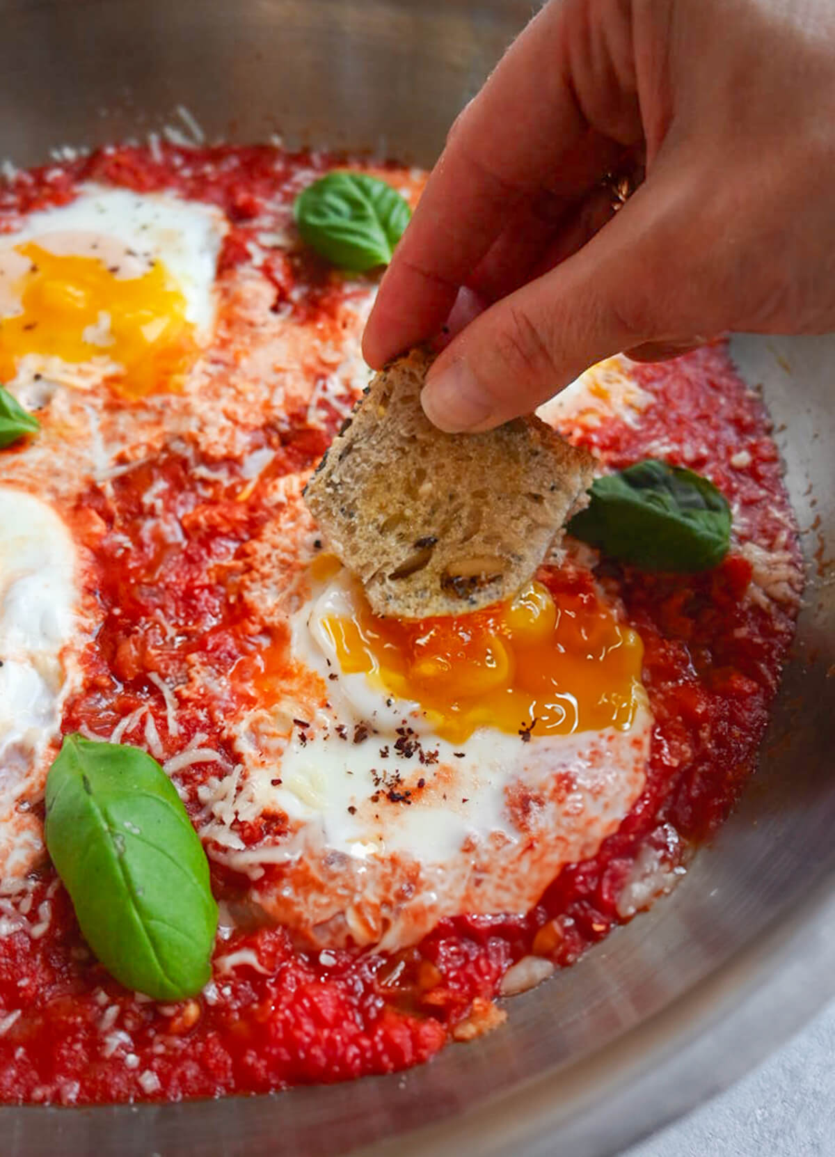 Une main tenant un morceau de pain dans des oeufs tomates.