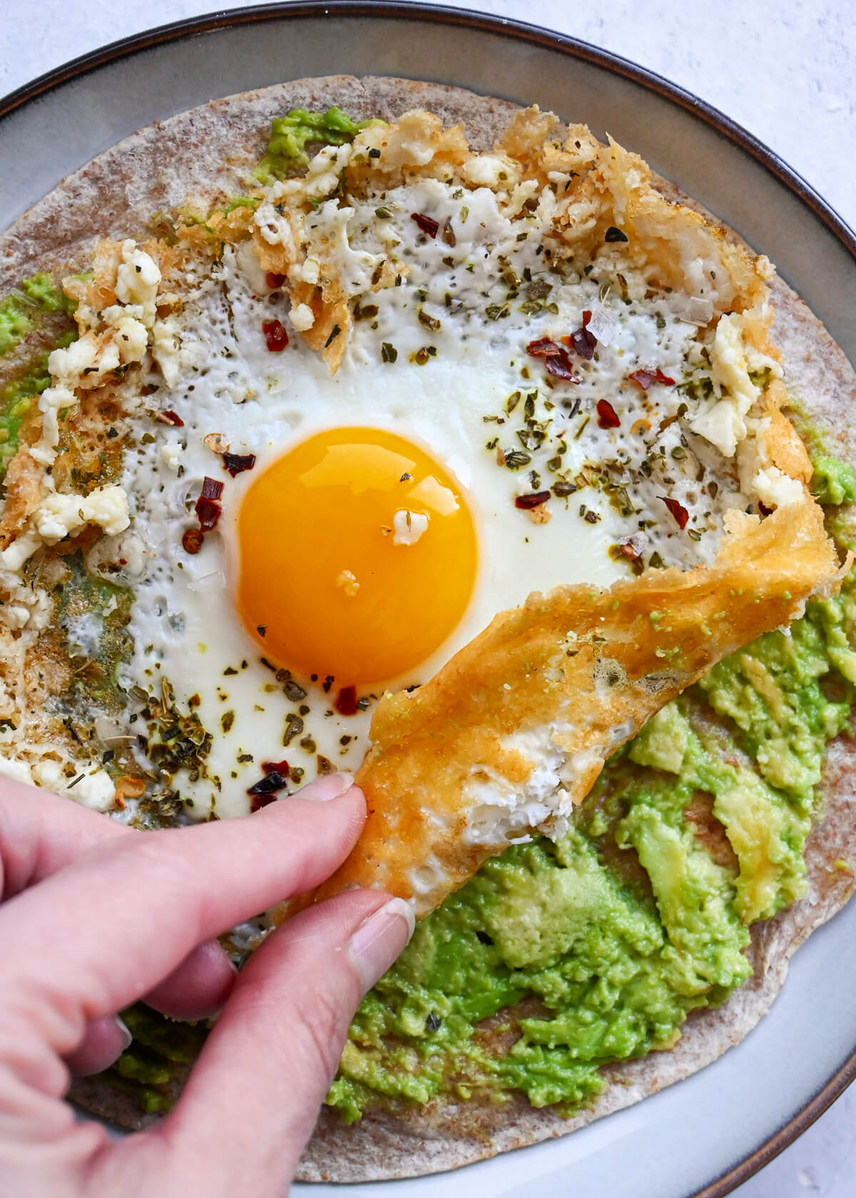 Une main tenant un morceau de feta frit avec un oeuf, et de l'avocat.