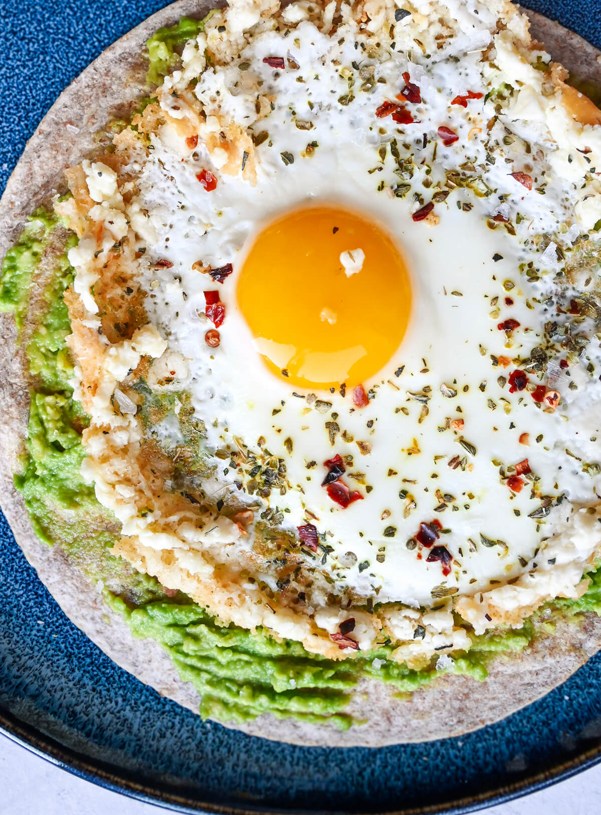 Un oeuf feta sur une tortilla avec un avocat, sur une assiette bleue.