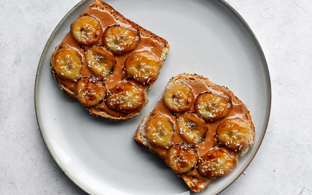 Deux tartines de beurre d'amande bananes caramélisées sur une assiette blanche.