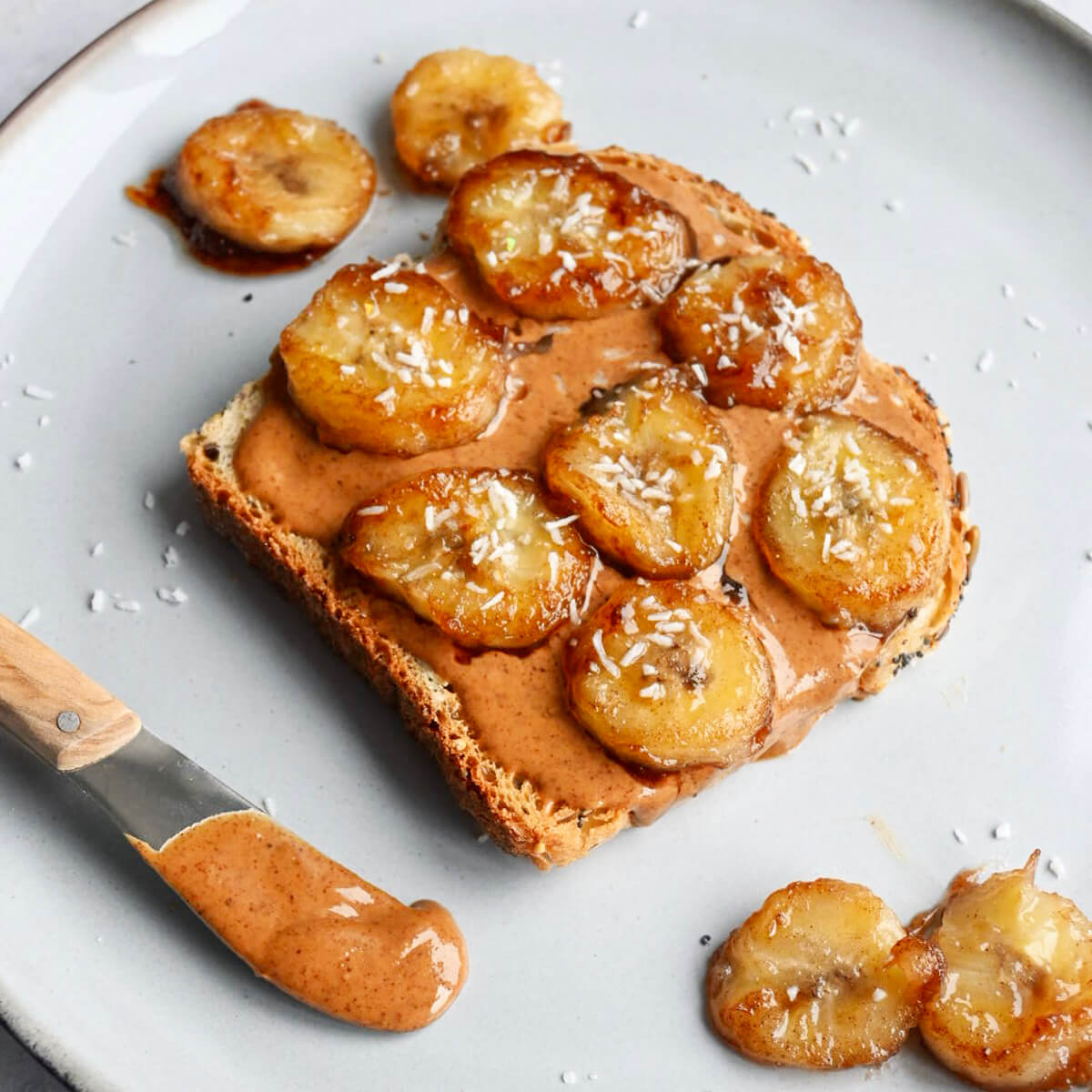 Une tartine beurre d'amande banane caramélisée sur une assiette blanche, couteau à beurre sur le côté.