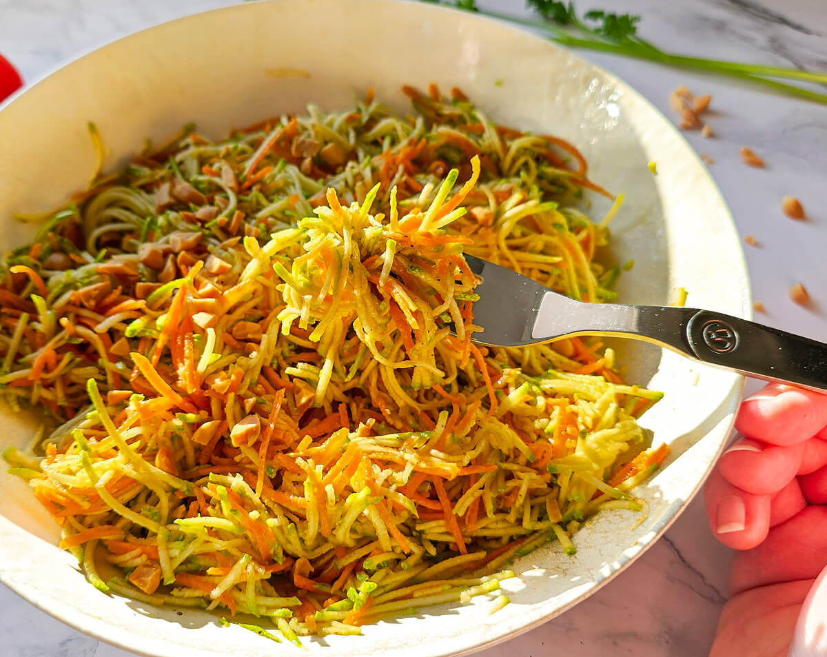 Une fourchette tenant un morceau de salade de Courgettes Carottes Râpées dans une assiette blanche.