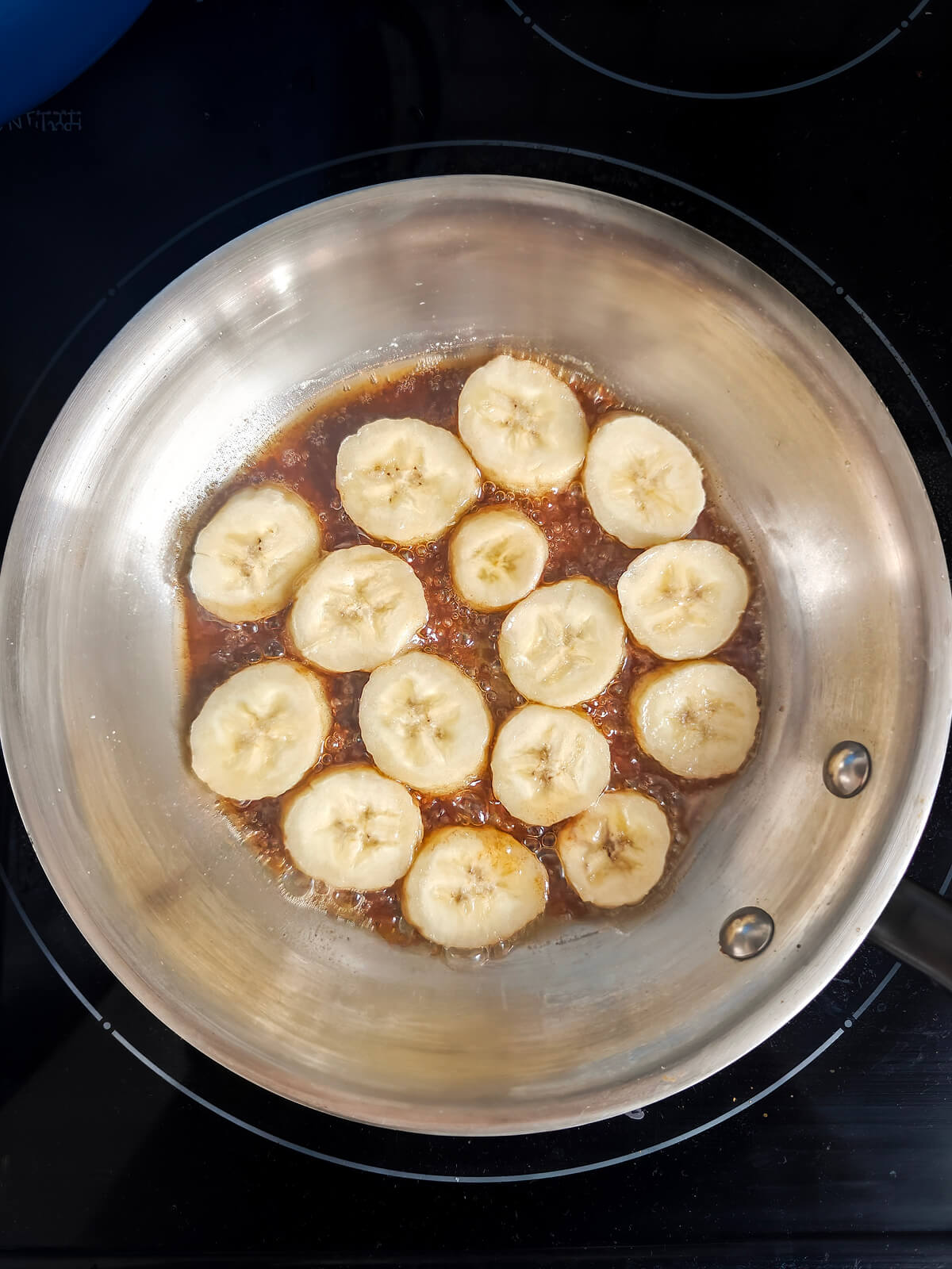 Des bananes en rondelles dans une poêle, sur un fond noir.