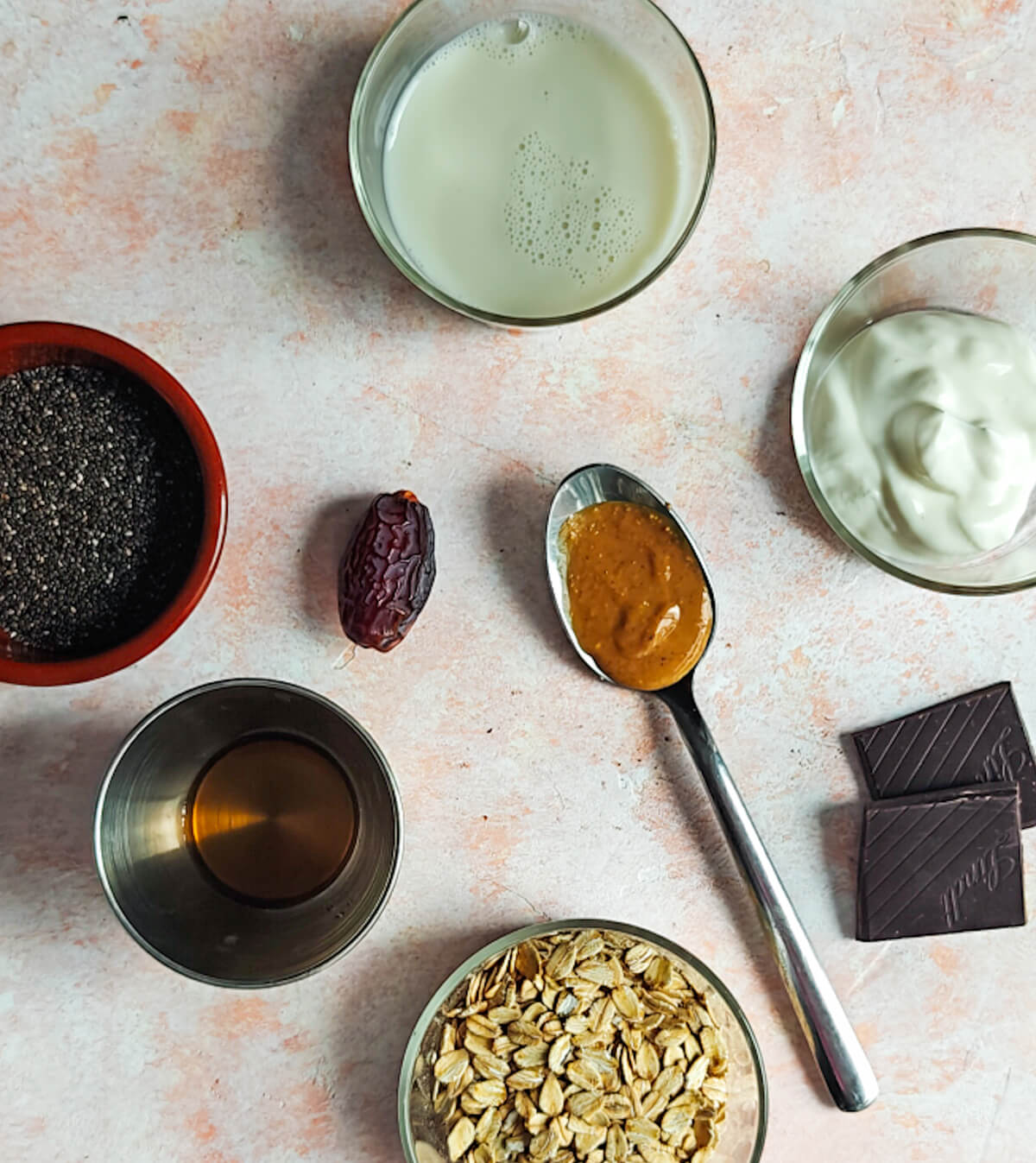 Des ingrédients pour un overnight oats snickers sur une surface rose claire.