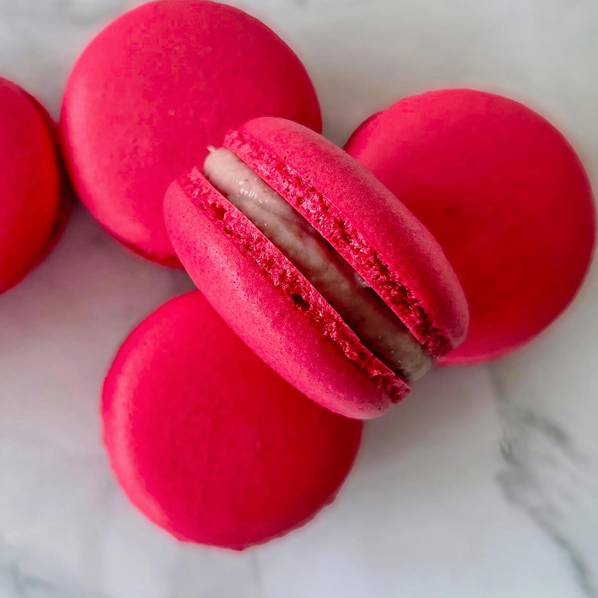 Des macarons à la framboise, ganache fondante sur un fond de couleur blanc marbré.
