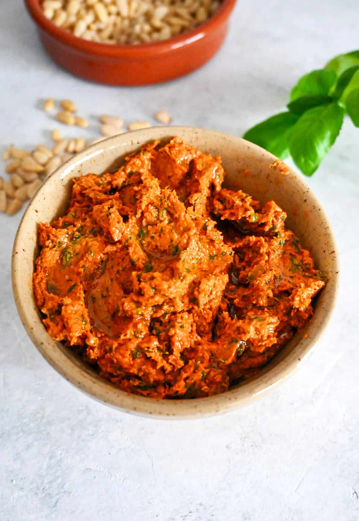 Du pesto rosso dans un bol, basilc et pignons sur le coté.