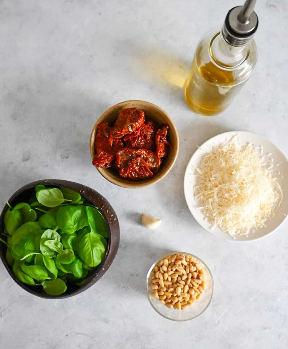 Des ingrédients pour une recette de pesto authentique sur un fond blanc gris.