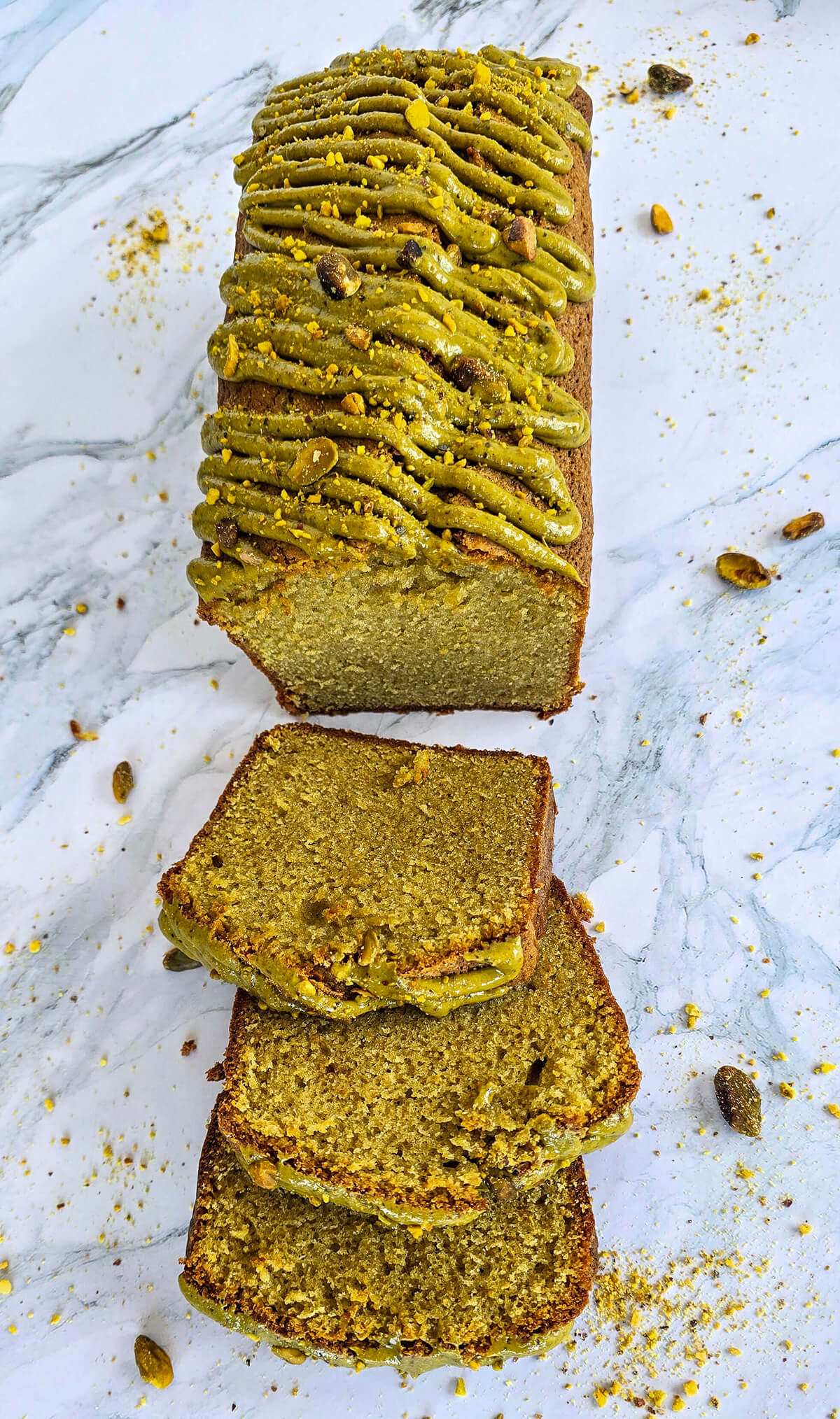 Un cake a la pistache coupé en tranches, sur une surface blanche marbrée.