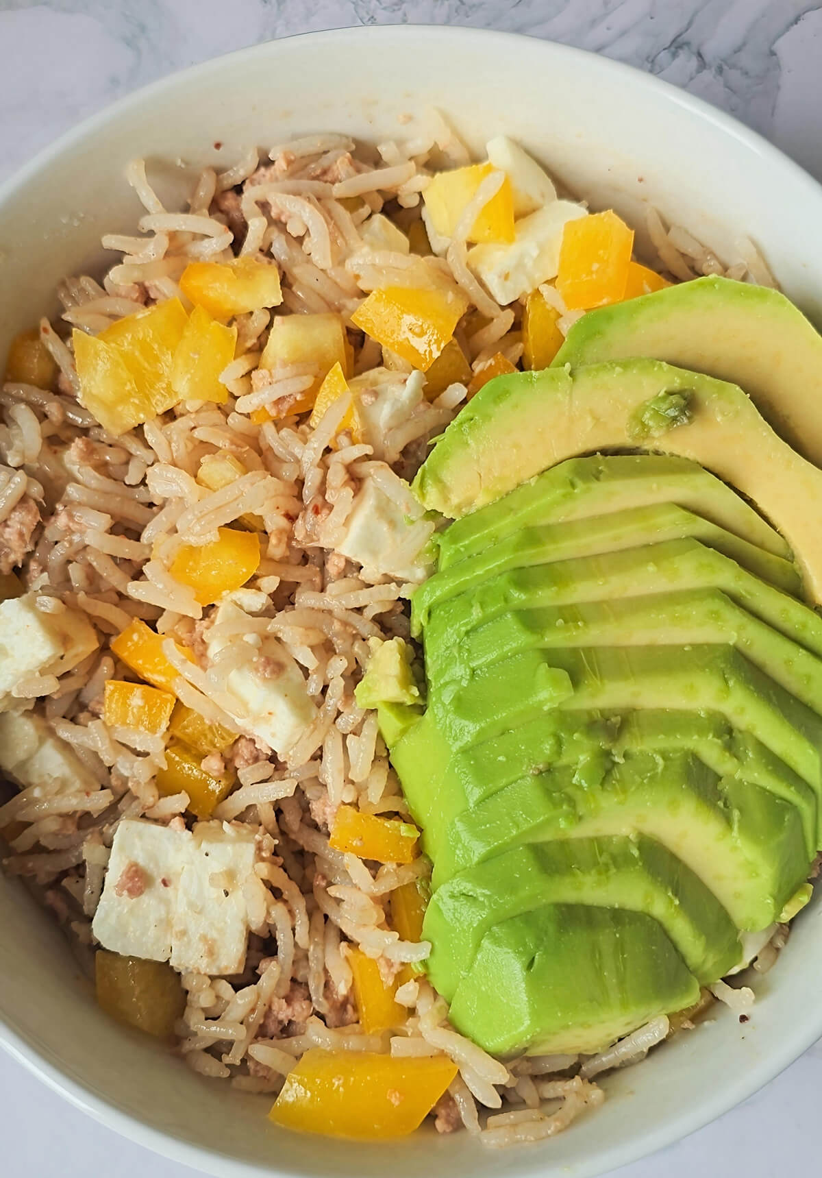 Une salade de riz au thon, avec morceaux de poivrons jaunes, et rondelles d'avocat.