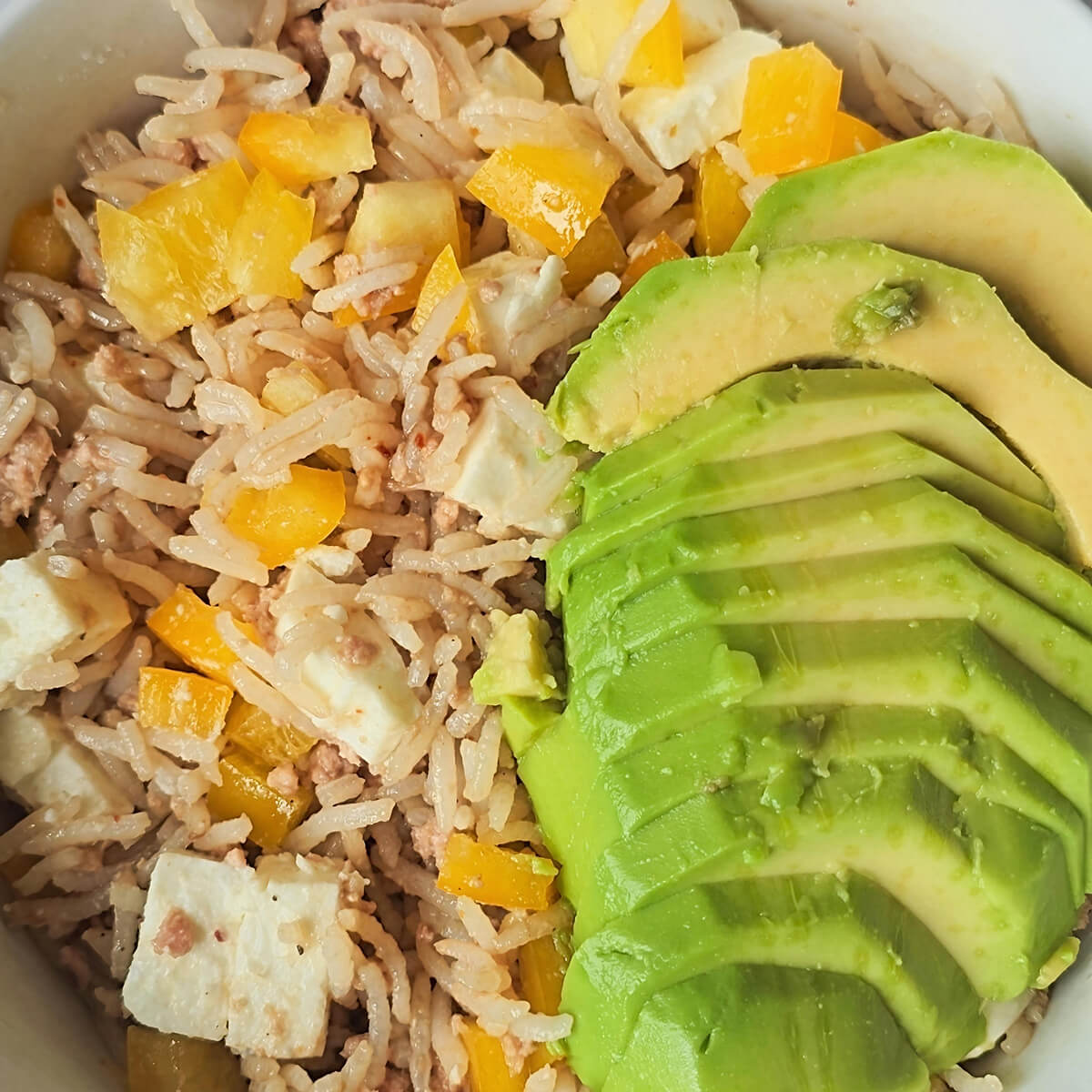 Une salade de riz au thon, avec morceaux de poivrons jaunes, et rondelles d'avocat.