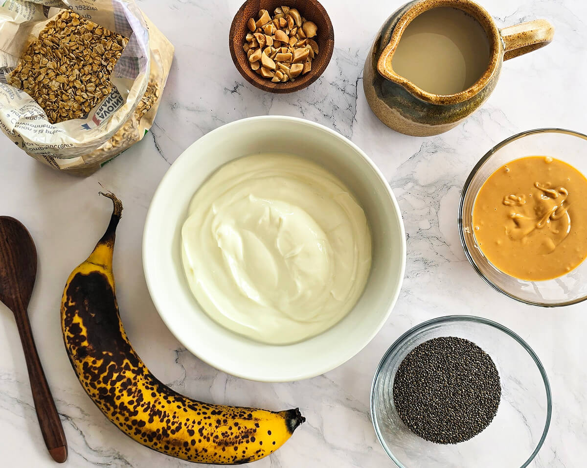 Des ingrédients pour une recette d'overnight porridge banane, sur un fond blanc marbré.