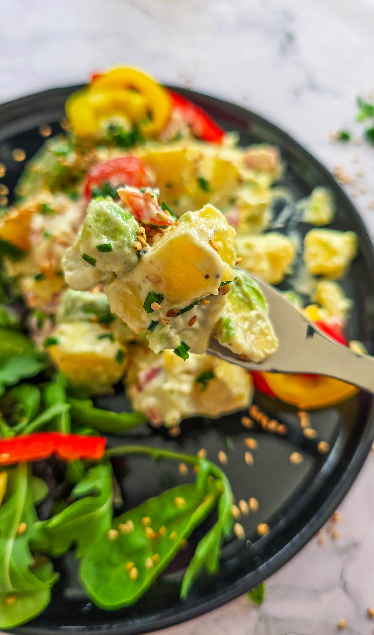 Une salade de pommes de terre dans une assiette noire, salade verte sur le coté.