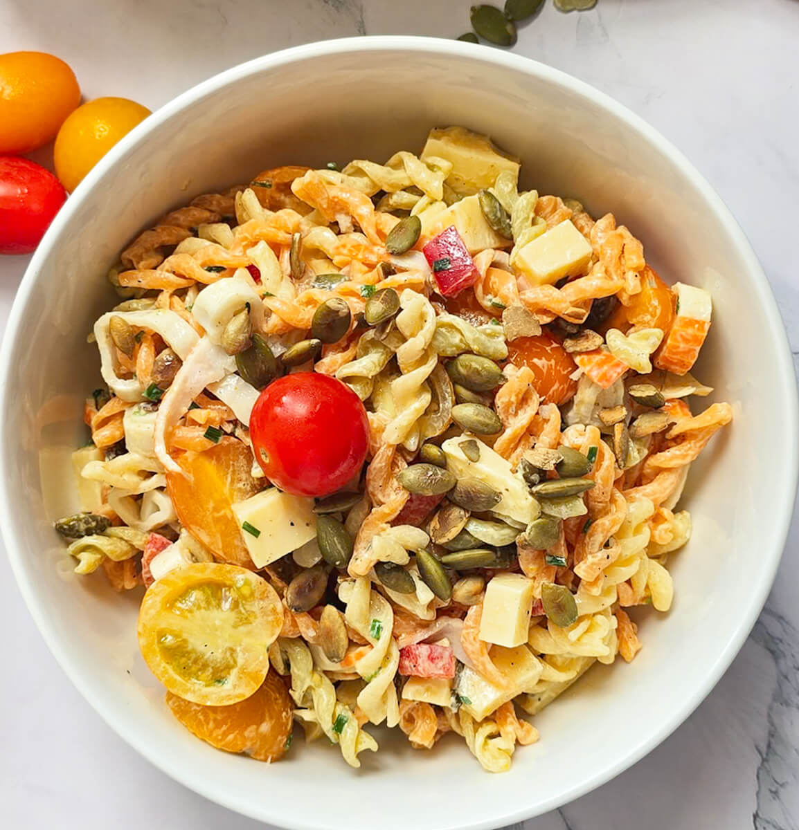 Une salade de pâtes avec surimi et tomates cerises dans un bol blanc.