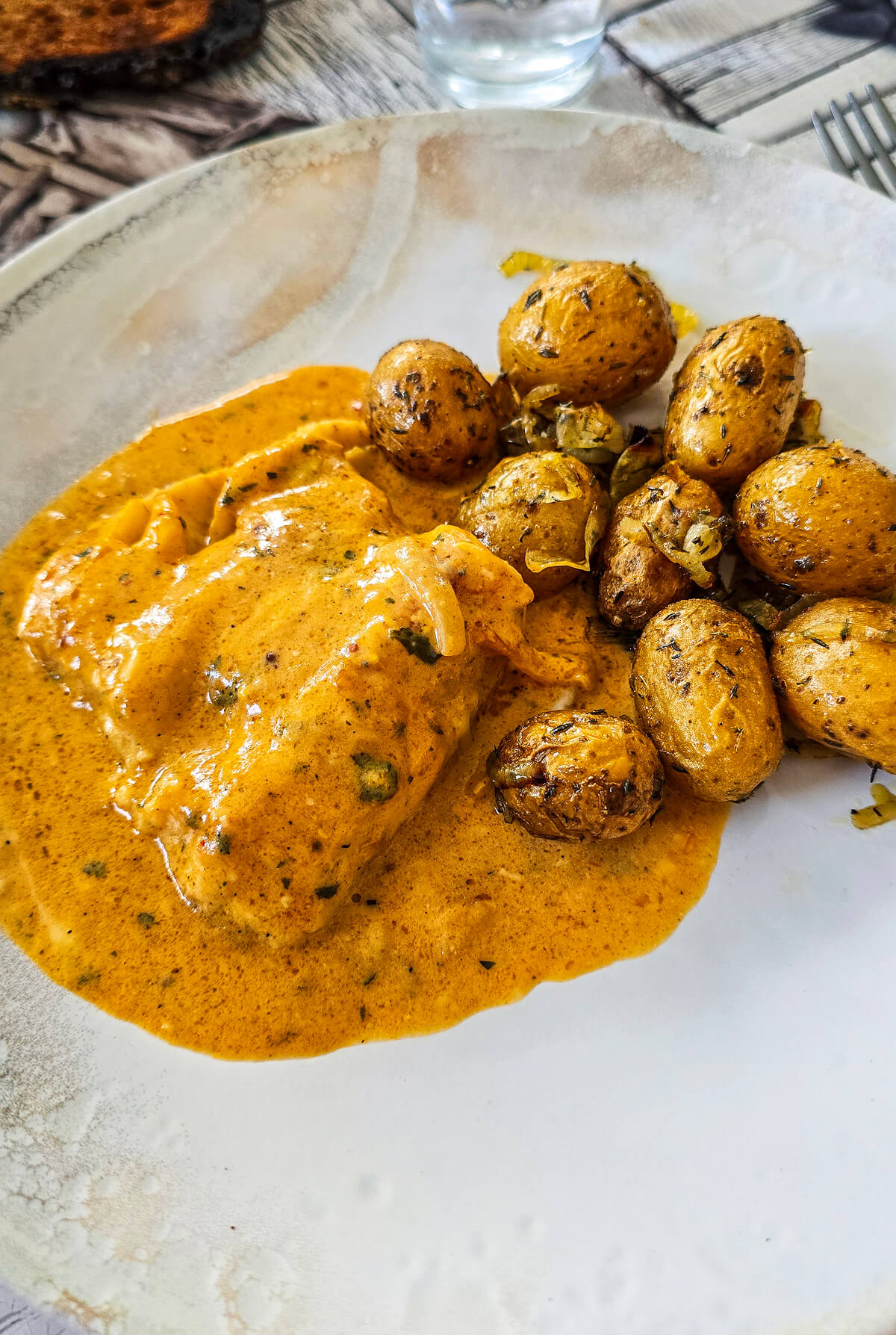 Des pommes de terre grenailles au airfryer, sur une assiette blanche avec un poulet en sauce.
