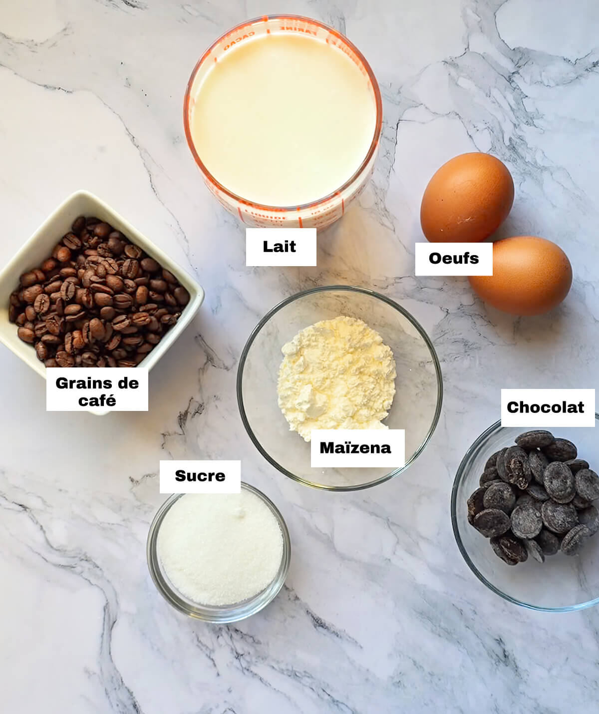 Des ingrédients pour une recette de crème chocolat café, sur un fond blanc marbré.