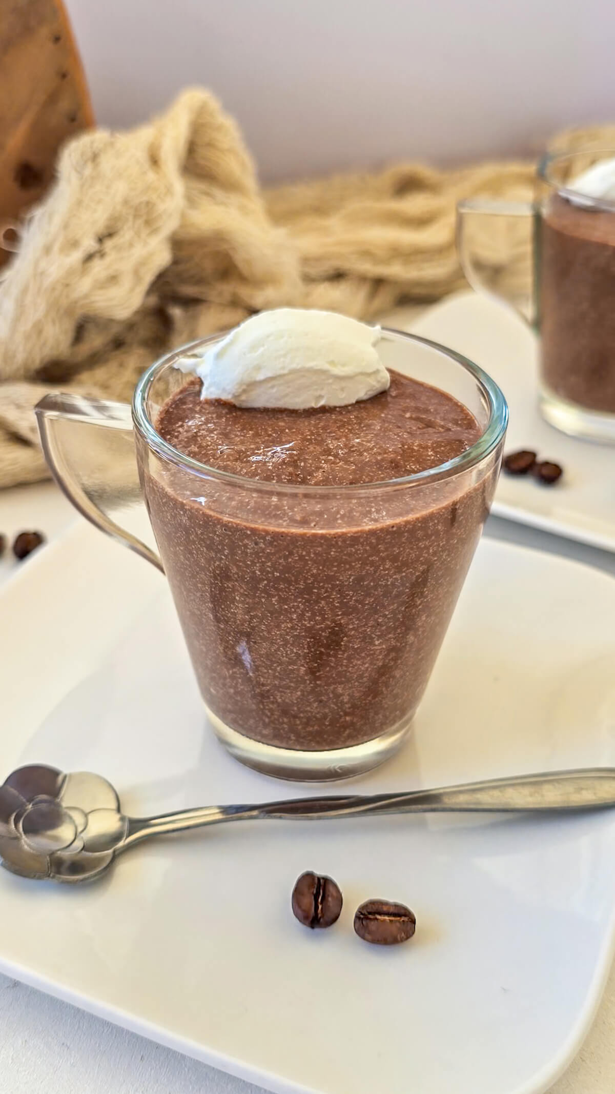 Une crème chocolat café dans une tasse en verre, sur une petite assiette avec petite cuillère.