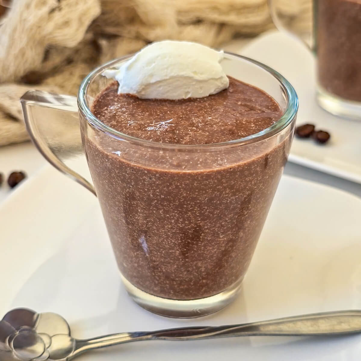 Une crème chocolat café dans un verre transparent, avec une touche de chantilly., petite cuillère sur le coté.