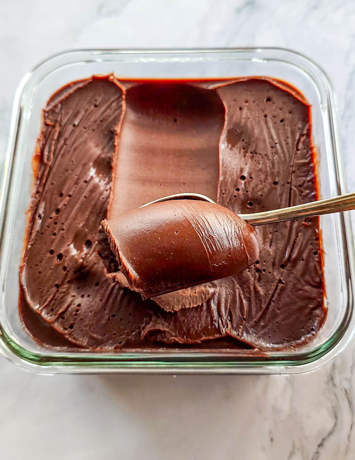 De la ganache au chocolat dans une boîte de conservation en verre, avec une cuillère qui enroule la ganache.