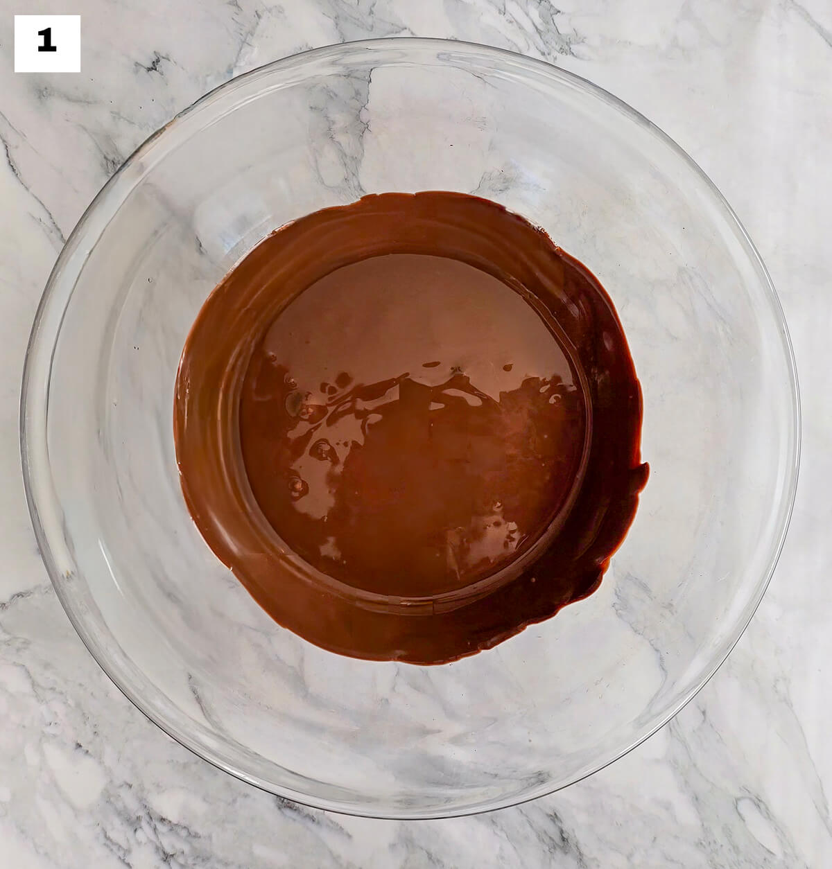 Du chocolat fondu dans un saladier en verre, sur un fond marbré.