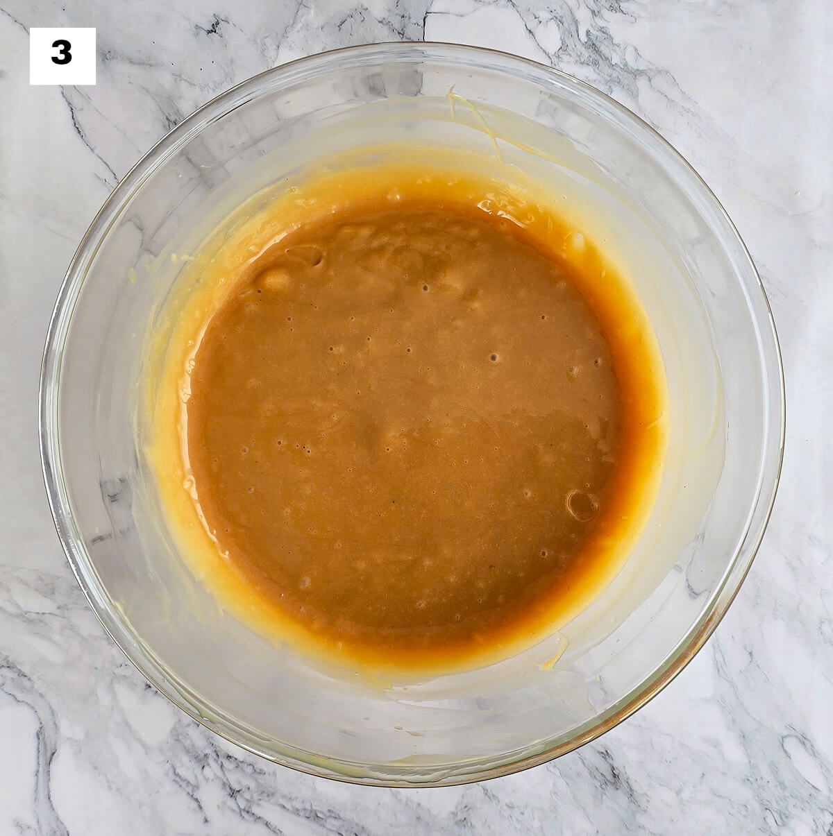De la ganache caramel beurre salé dans un saladier en verre, sur une surface blanche marbré.