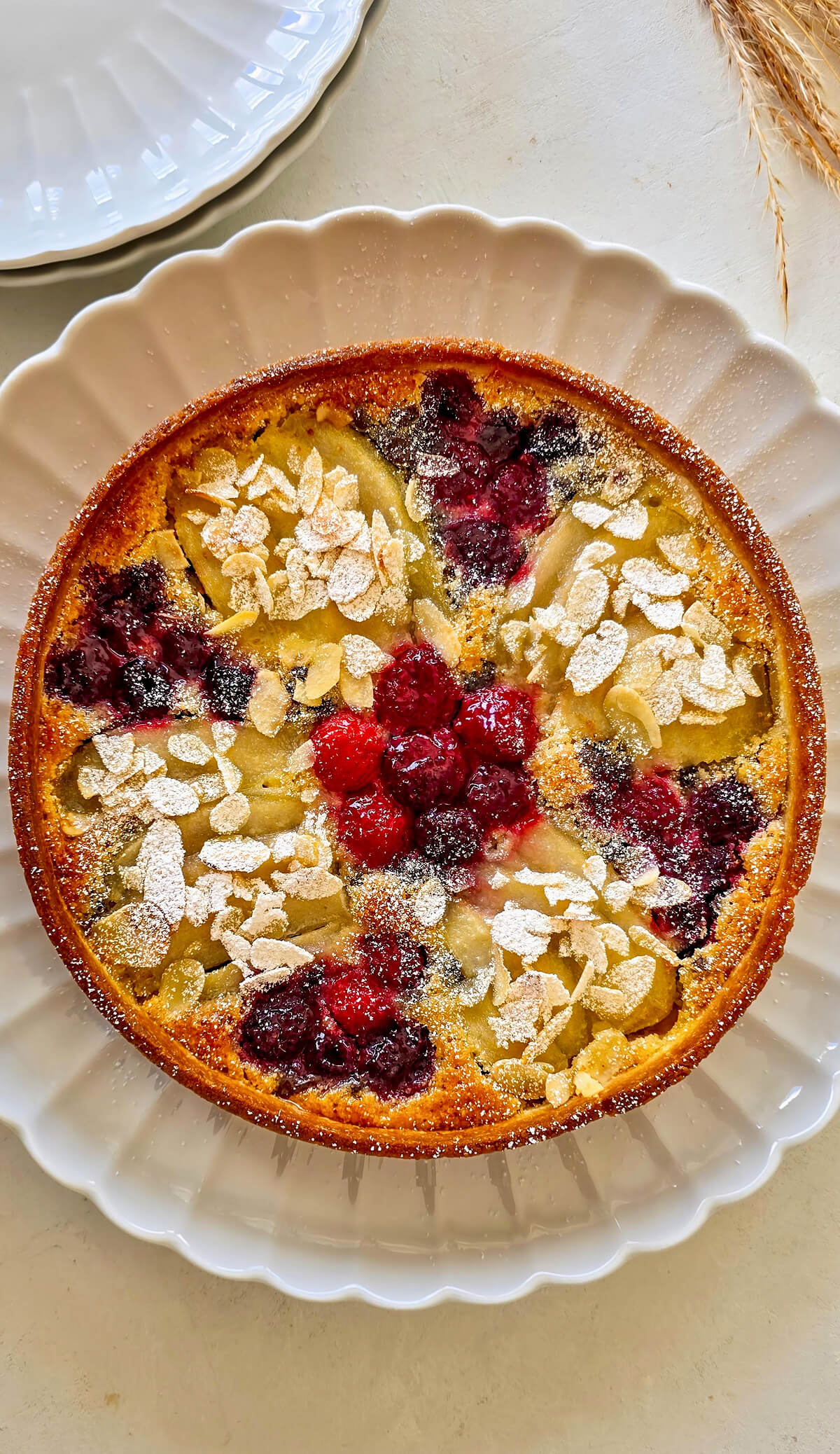 Une tarte amandine poire framboise sur une assiette blanche.