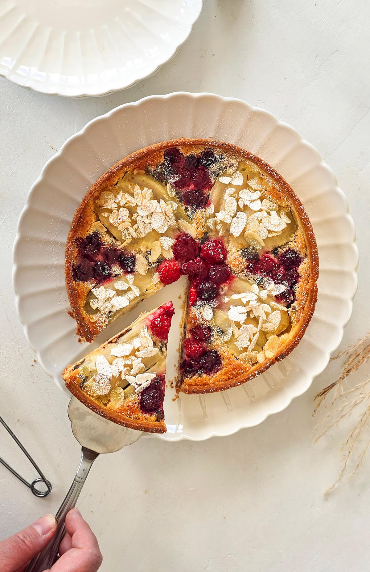 Une tarte amandine poire framboise sur une assiette blanche avec une spatule.