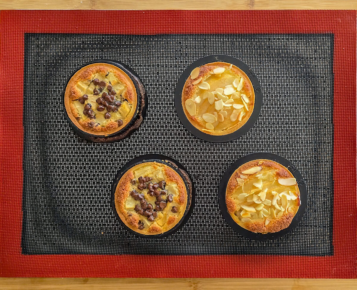 Des tartelettes poire amandine sur une plaque de cuisson en silicone noire et rouge, après cuisson.