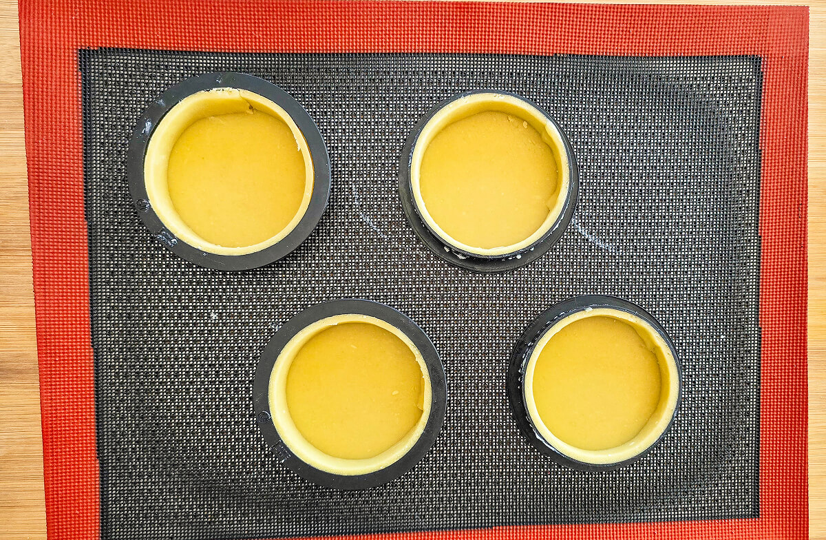4 cercles à pâtisseries sur une feuille en silicone, avec de la pâte sucrée pour faire des tartelettes poire amandine.