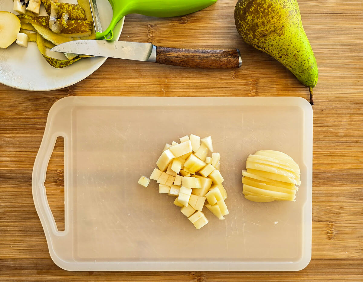 Une planche à découper blanche avec des morceaux de poire, un couteau, et une poire entière, sur un fond en bois.