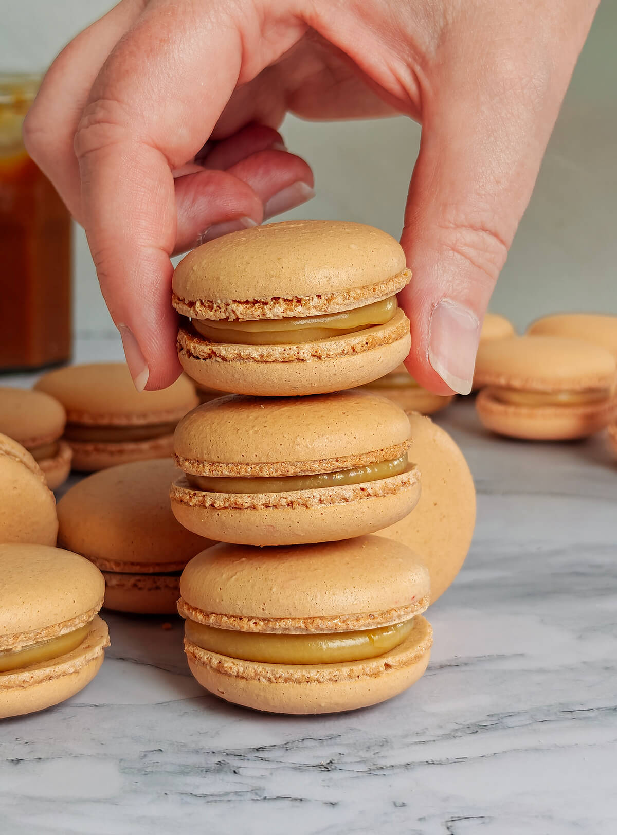 Une main tenant un macaron caramel beurre salé, sur un deux autres macarons.