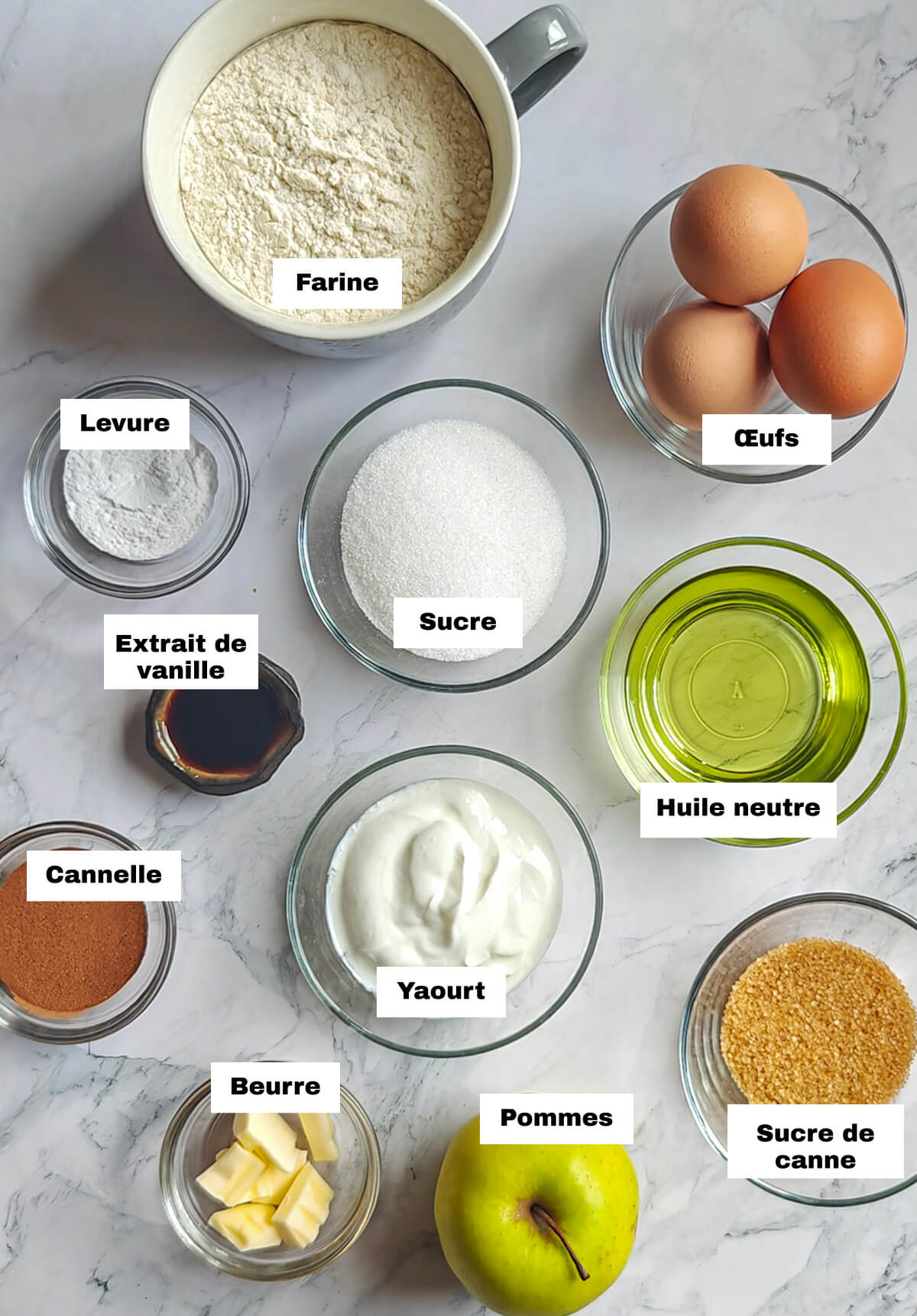 Des ingrédients pour une recette de muffins pommes cannelle sur un fond blanc.