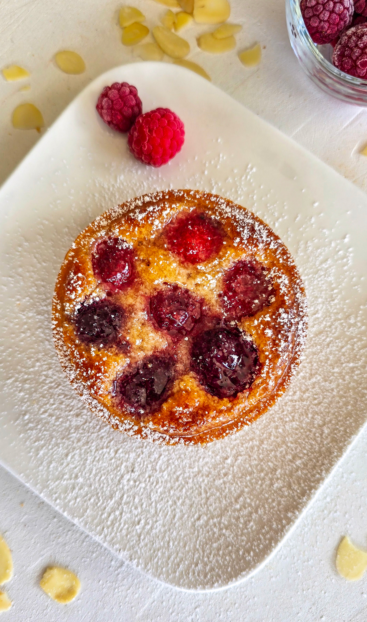 Une tartelette framboise sur une assiette blanche, avec un peu de sucre glace. et des amandes éffilées. 