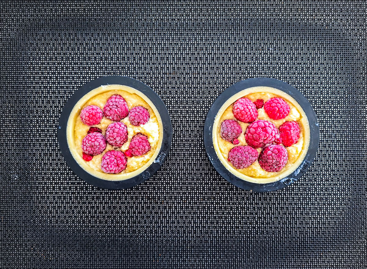Deux tartelettes aux framboises crues dans leurs cercles à pâtisserie, sur une feuille de silicone.