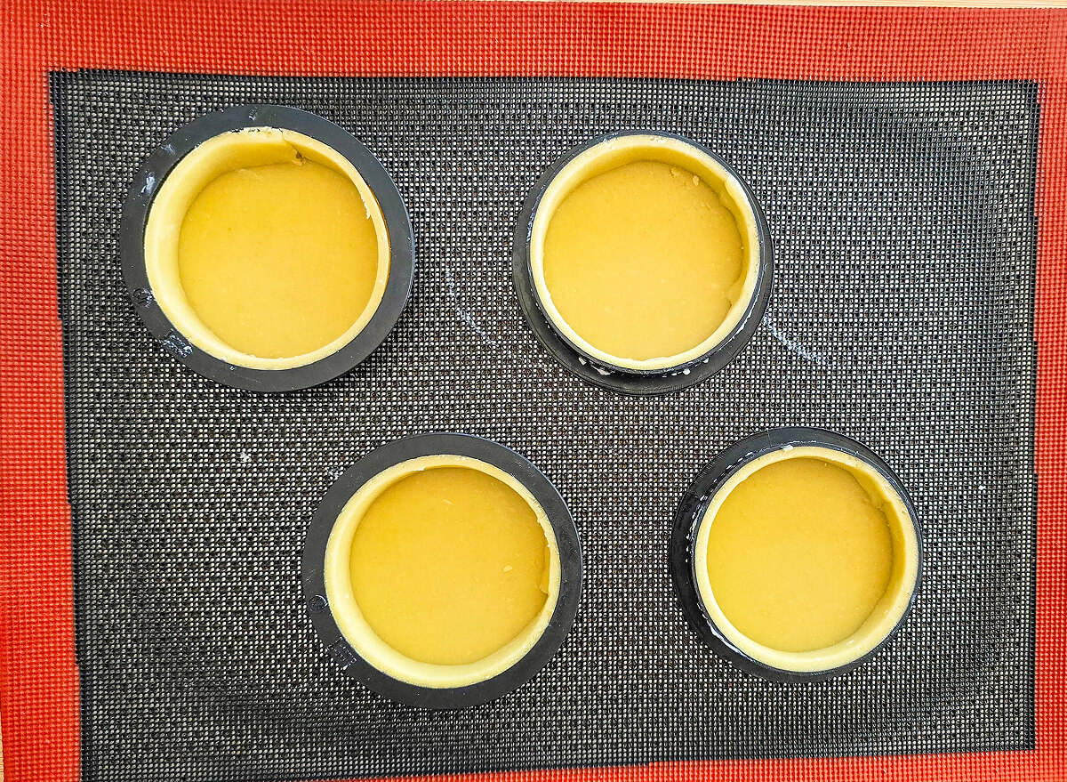 4 cercles à pâtisseries sur une feuille en silicone, avec de la pâte sucrée pour faire des tartelettes.